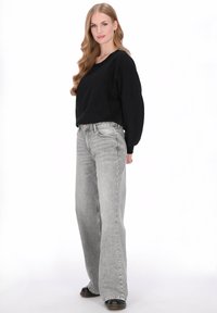 Zwarte top met lange mouwen, een losse pasvorm en een brede halslijn, gecombineerd met hooggehate, lichtgrijze wijde jeans en zwarte laarzen.