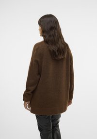 Brown oversized sweater made of a soft, textured knit. Long sleeves and a relaxed fit, paired with shiny black leather pants.