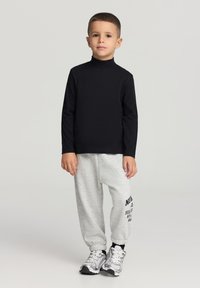 Czarna dopasowana koszulka z długim rękawem, jasnoszare spodnie dresowe z czarnym nadrukiem oraz sportowe szare trampki. Prosty, codzienny strój dla dzieci.