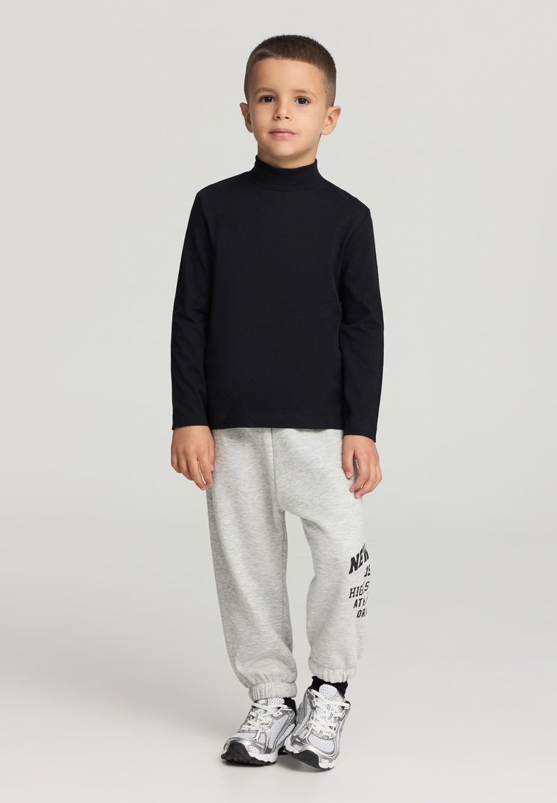 Czarna dopasowana koszulka z długim rękawem, jasnoszare spodnie dresowe z czarnym nadrukiem oraz sportowe szare trampki. Prosty, codzienny strój dla dzieci.