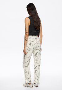 Top corto negro con ribetes y acentos de tachuelas, combinado con pantalones off-white con un patrón de salpicaduras. Llevado con zapatillas plateadas.