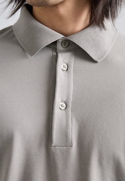 Šedá polo tričko vyrobené z měkké látky, s rozepnutým límcem a tří knoflíkovou légou s šedými knoflíky se čtyřmi otvory, ukazující hladkou strukturu.