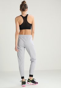 Sujetador deportivo negro de malla con diseño de espalda cruzada, combinado con pantalones de chándal grises claros ajustados que tienen una cinturilla negra y dobladillos acampanados, y zapatillas de colores.