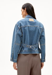 Jeansjack met een lichtblauwe wassing, voorzien van een merklabel op de rug, gestructureerde schouders en een verstelbare tailleband.