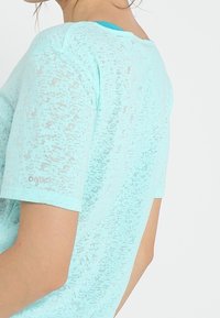 Ljusblå, texturerad kortärmad skjorta med en något genomskinlig look och rund halsringning, med subtila mönster.