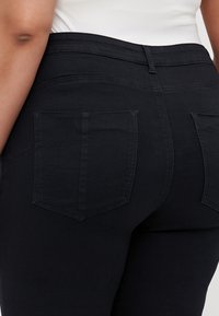 Jeans de mezclilla negra con un diseño ajustado, que cuentan con dos bolsillos traseros, detalles de costura sutiles y una textura suave.