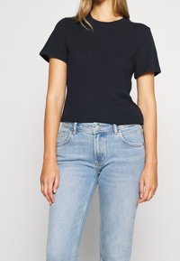 Navy modrá bavlněná trička s krátkým rukávem, kulatým výstřihem a volným střihem, v kombinaci se světle modrými džínami s klasickým designem.