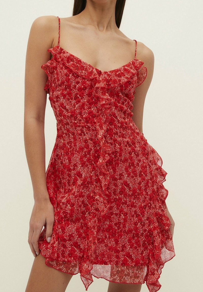 Abito rosso a fiori realizzato in tessuto leggero, con spalline sottili, dettagli arricciati lungo il collo e l'orlo, e una silhouette fluida.