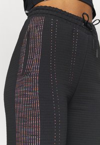 Schwarze, strukturierte Hosen mit elastischem Bund und mehrfarbigem, senkrechtem Streifenmuster entlang der Seitennaht und der Taschenöffnung.