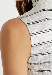 Top senza maniche bianco e strutturato con righe orizzontali nere. Collo alto con leggere scanalature. Tessuto liscio con una forma aderente.
