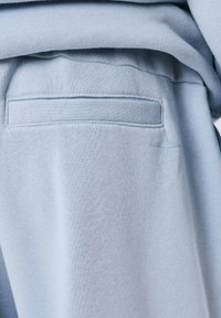 Le tissu du sweat-shirt bleu clair présente une texture lisse, avec une petite poche au dos et un détail étoile discret de couleur assortie.