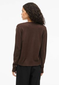 Bruine gebreide trui met geribde manchetten en zoom, met een eenvoudig ontwerp en zachte textuur, weergegeven vanaf de achterkant op een model.