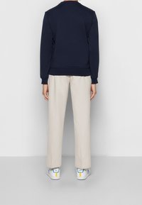 Námořnická mikina s kulatým výstřihem, béžové kalhoty a bílé tenisky s modrými a žlutými akcenty, viděné ze zadní strany. Hladká textura látky.