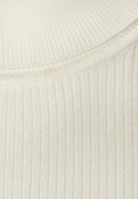 Rippendes cremfarbenes Strickgewebe mit einer weichen Textur. Verfügt über einen enganliegenden Ausschnitt und einen subtilen Glanz im Material, der seine Dehnbarkeit betont.