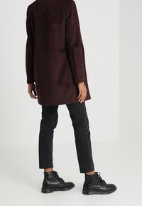 Burgunderfarvet uldfrakke med lige silhuet, kombineret med sorte straight-leg jeans og sorte snørede ankelstøvler.