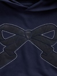 Tumesinine kapuutsiga pluus, millel on suur, tekstureeritud musta lipsu disain, mille ääres on väikesed hõbedased nupud, luues dekoreeritud keskpunkti.