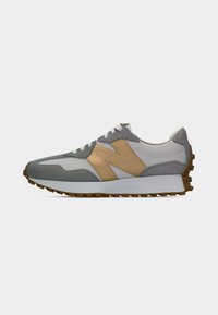 Lichtgrijze en witte sneaker met een beige "N"-logo, witte veters en een bruine, gestructureerde zool, weergegeven in zijprofiel van rechts tegen een witte achtergrond.