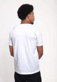 T-shirt bianca in cotone con collo rotondo e maniche corte, caratterizzata da una texture liscia e una vestibilità comoda, vista da dietro.