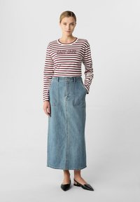Gonna di jeans lunga di colore azzurro chiaro con tasche frontali. Abbinata a una maglietta a maniche lunghe a righe con una grafica e scollo rotondo. Scarpe nera a sandalo con tacco.