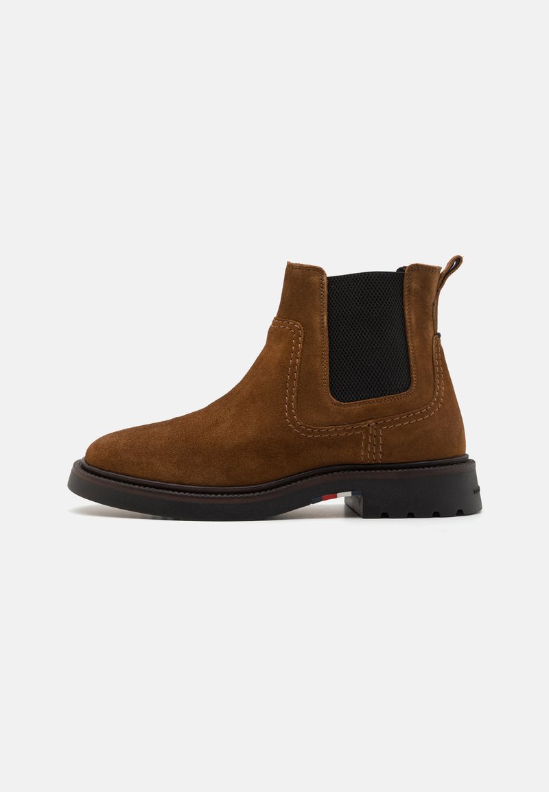 Botine din suede maro, cu panouri elastice pe laturi, talpă din cauciuc plat și accente de cusătură contrastante. Include un tab pentru a facilita îmbrăcarea.