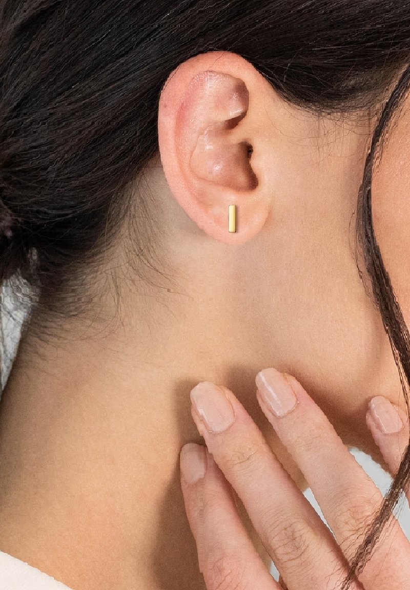 Zlaté obdĺžnikové puzdrové náušnice nosené na prepichnutom uchu. Hladký, minimalistický dizajn s lesklým povrchom. Na pozadí je viditeľná pokožka.