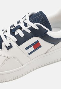 Sneaker bianco e navy realizzato in pelle e tessuto, con una linguetta navy testurizzata, lacci bianchi e una toppa rettangolare con logo.