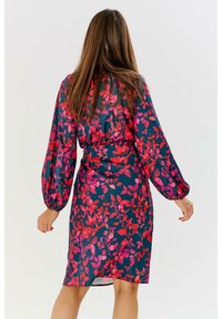 Květinové šaty s tmavým pozadím, s jasně červenými a růžovými vzory listů, dlouhými nafouknutými rukávy a detailem stahování v pase.