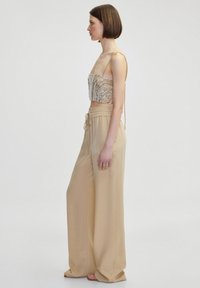 Beaded crop top with intricate patterns and thin straps, paired with high-waisted, wide-leg beige trousers made of smooth fabric.