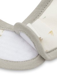 Close-up van een beige stoffen band met een witte klittenbandsluiting die gedeeltelijk open is op een lichtgekleurde textielachtergrond.