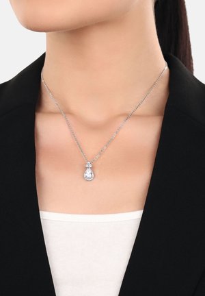 Donna che indossa una collana in argento con un pendente a forma di goccia d'acqua in pietra trasparente sopra una maglietta bianca e un blazer nero.