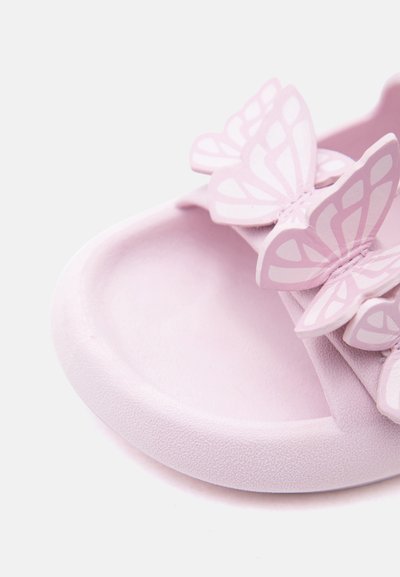 Ανοιχτό ροζ σαμπό με τρεις διακοσμητικές πεταλούδες στο λουρί, απεικονίζοντας κοντινή λήψη της υφής της σόλας και της περιοχής των δακτύλων.