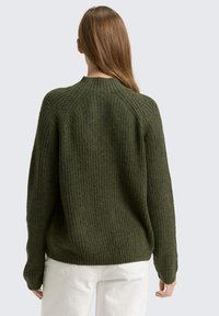 Dunkelgrüner, gerippter Pullover mit hohem Kragen, Raglanärmel und lockerer Passform. Das Material wirkt strukturiert und gestrickt.