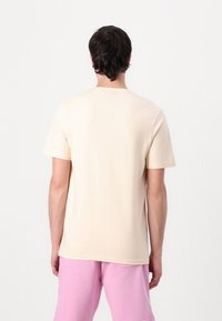 Beige t-shirt med kort ärm i mjukt tyg, rund halsringning och avslappnad passform, tillsammans med ljusrosa shorts. Minimalistisk design.