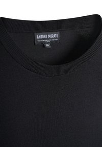 Maglione nero slim-fit realizzato in un misto viscosa. Presenta un colletto a coste. L'etichetta mostra il nome del marchio e le informazioni sui tessuti.