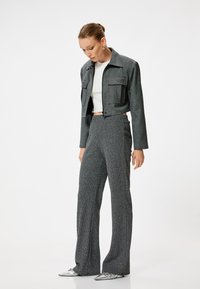 Chaqueta gris corta con dos bolsillos frontales, combinada con pantalones de campana grises de cintura alta. La modelo lleva una blusa blanca y zapatos plateados.