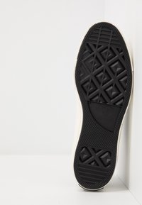 Czarna gumowa podeszwa trampka z geometrycznym wzorem bieżnika i logo „Converse All Star” na białym tle.