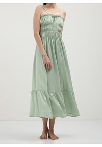 Robe vert menthe, longueur cheville, avec bretelles spaghetti, corsage smocké et ourlet à volants à étages. Texture douce, design décontracté.