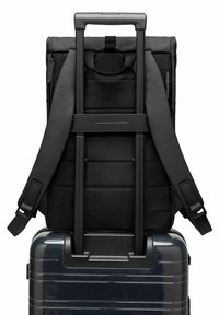 Sac à dos noir avec texture rembourrée et bretelles ajustables monté sur une valise élégante, gris foncé, avec surface lisse et lignes horizontales.