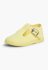 Scarpa di tela gialla con punta chiusa, design a T-strap, fibbia regolabile e suola in gomma flessibile. Cuciture in vista sulla tomaia.