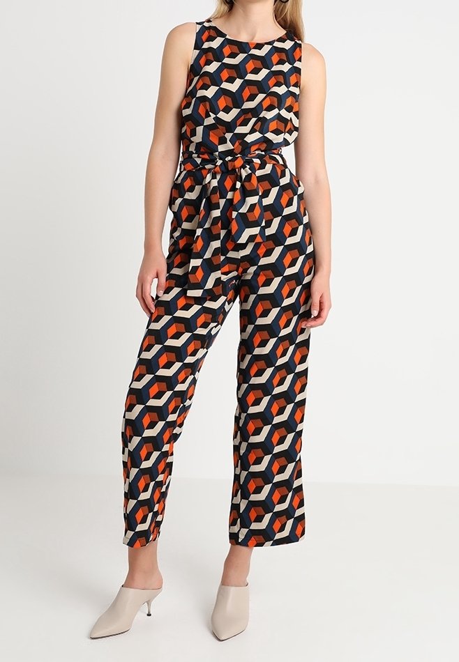 Combinaison sans manches avec un motif géométrique en rouge, beige et noir. Détail de taille nouée, design à jambes larges et tissu léger.