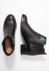 Botas negras de cuero hasta el tobillo con una superficie texturizada, un cierre de cremallera en un lado y un tacón apilado. Diseño elegante y funcional.