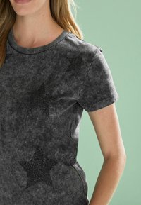 Sort, kortærmet t-shirt med en blød, tekstureret overflade og glitrende sorte stjernemønstre på forsiden. Rund halsudskæring og afslappet pasform.
