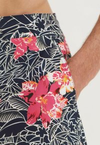 Blumen-Shorts mit navyblauem Hintergrund, die große pinke Blumen und weiße tropische Blättermuster zeigen. Inklusive Seitentaschen.