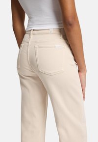 Jeans en jean beige à coupe droite, dotés de deux poches arrière et de détails de couture subtils. Conçus avec une taille mi-haute.