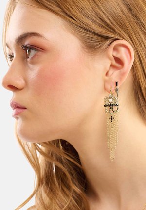 Boucles d'oreilles dorées avec des chaînes cascade, présentant des accents noirs et un détail en perle, mettant en valeur des embellissements complexes et un design unique.