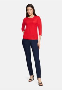 Czerwony, teksturowany sweter z rękawami do łokcia, w połączeniu z ciemnoniebieskimi dopasowanymi dżinsami i czarnymi sandałami na obcasie z paskami. Prosty, dopasowany fason.
