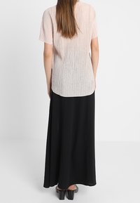 Světle růžový plisovaný top s krátkými rukávy v kombinaci s černou maxi sukní. Tento outfit se vyznačuje splývavým designem a texturovaným povrchem.