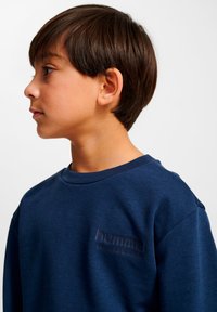 Marinblå sweatshirt i mjukt tyg med rund halsringning, med en texturerad "hummel"-logotyp på bröstet och en avslappnad passform.