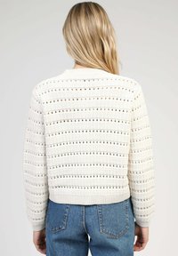 Pull en tricot blanc cassé avec un motif à rayures horizontales et des détails en dentelle. Il présente un col et un ourlet côtelés, associé à un jean bleu.