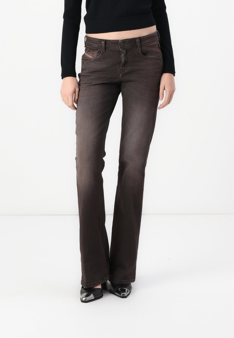 Brown flared jeans with a subtle faded texture, five-pocket design, and a button closure. Paired with black shoes featuring a glossy accent.